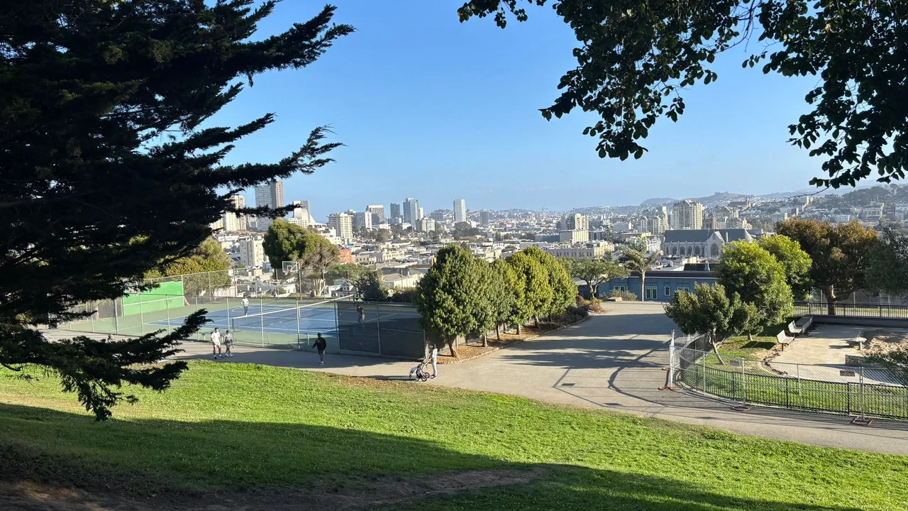 Tennis courts below a grassy slope with the San Francisco skyline beyond