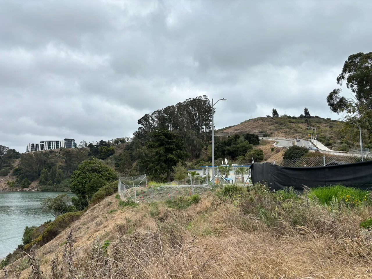 A fenced, partly planted hillside overlooks the water at the future Chapel Grove park site.