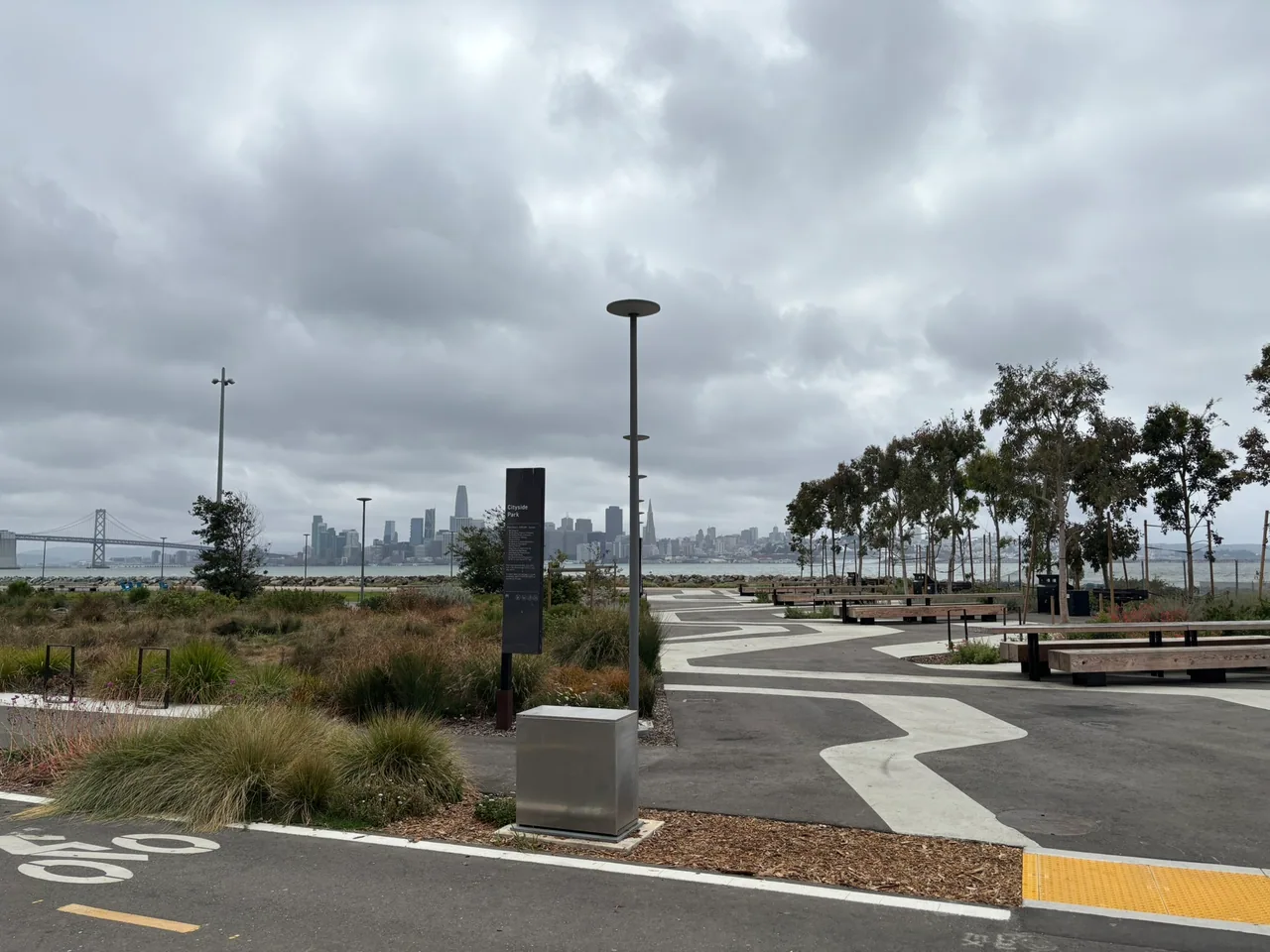 A modern play area, curved paths, and young landscaping with the San Francisco skyline in the distance.