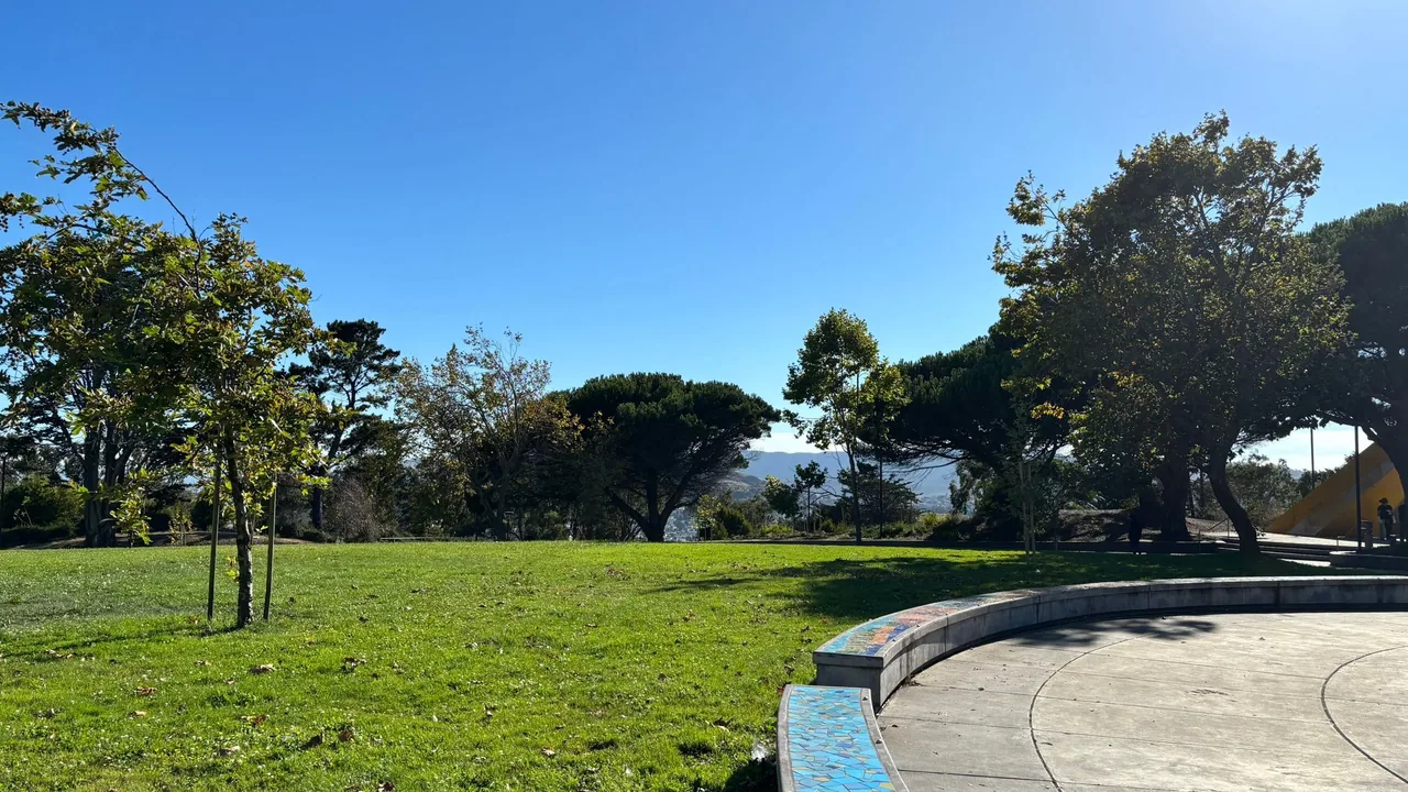 Green lawn and curved mosaic-tiled bench overlooking trees and the hillside