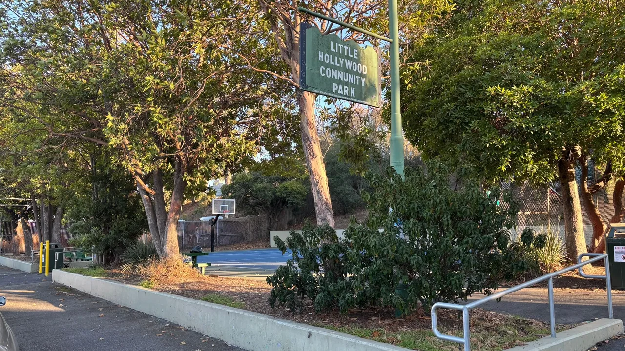 Little Hollywood Community Park sign above a tree-lined entrance and basketball court