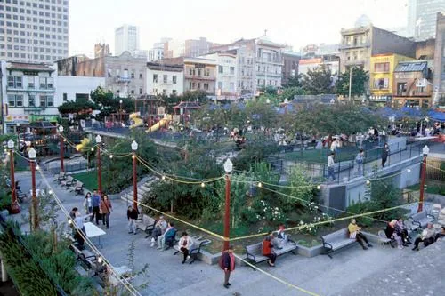 An elevated view across Portsmouth Square showing curved paths, benches, trees, play areas, and surrounding Chinatown buildings.