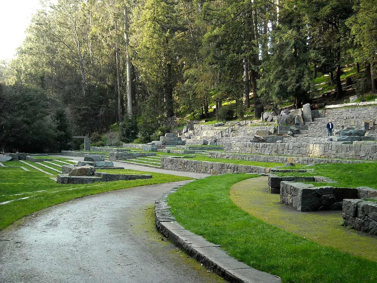 Curving paths pass stone terraces and grass seating areas surrounded by tall trees at Stern Grove.