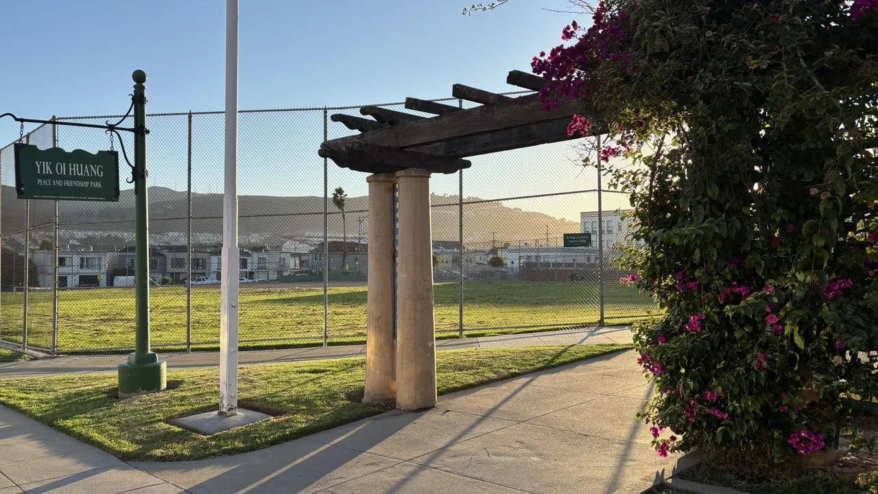 Park sign and wooden pergola beside a fenced grassy playing field